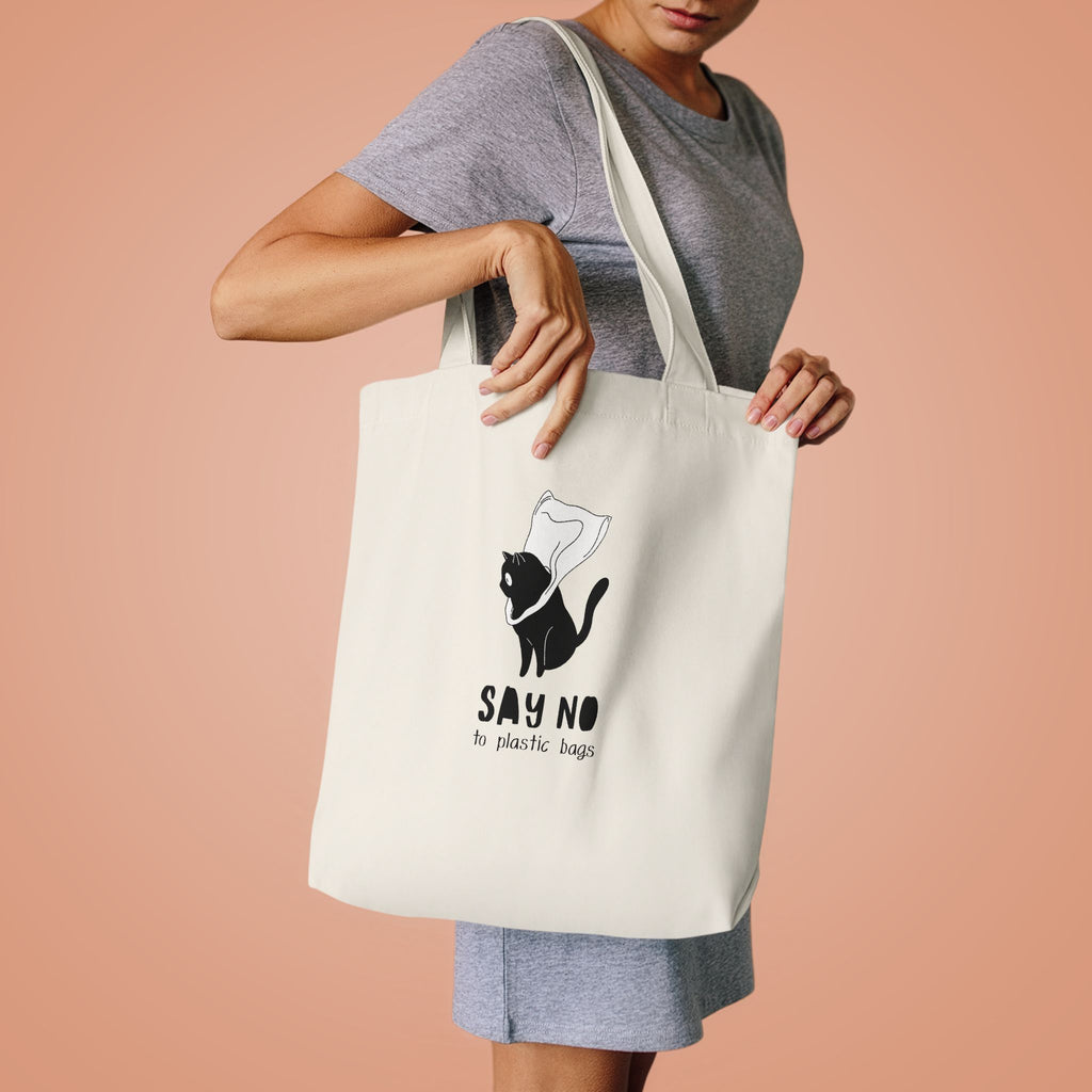 Woman in a grey tee lifting the Say No to Plastic Bags tote by its handles against peach