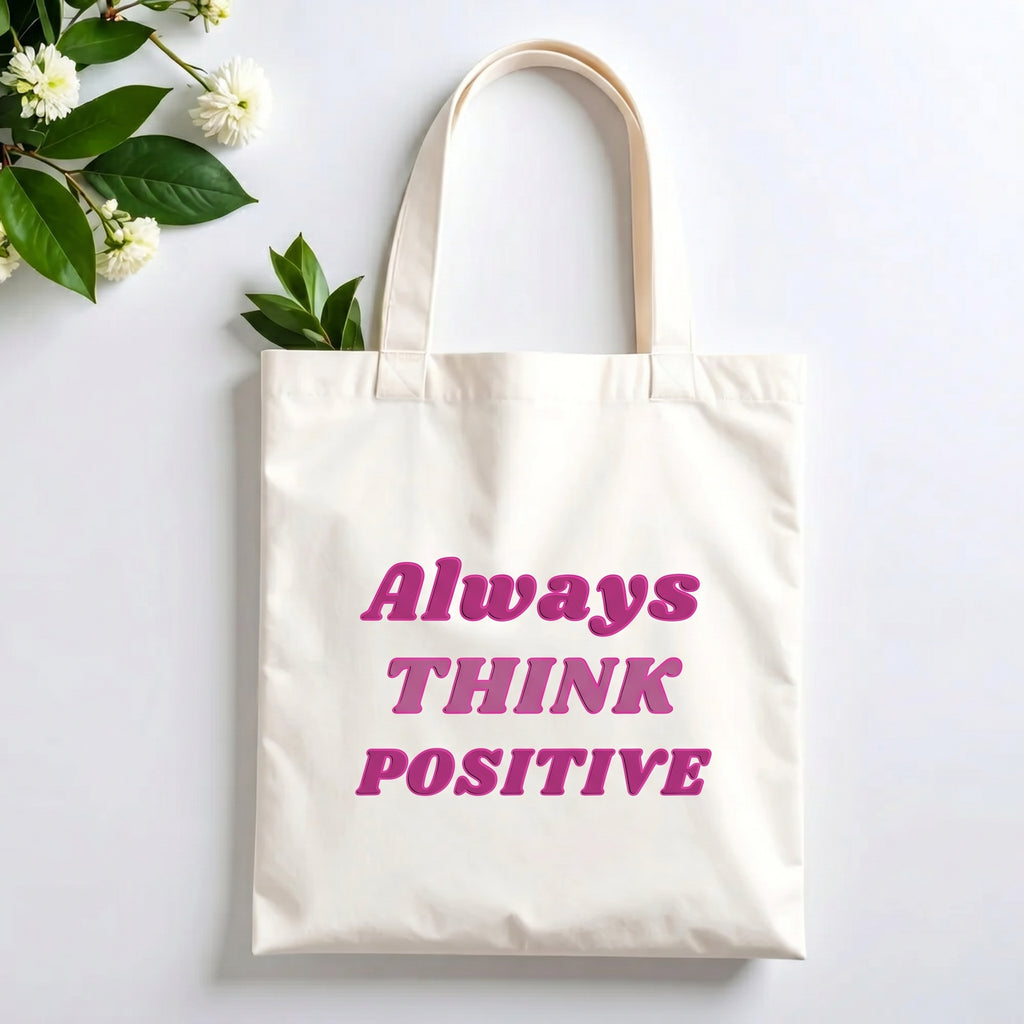Plovera Co Always Think Positive tote laid flat on pale grey with white blossom and green leaves