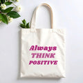 Plovera Co Always Think Positive tote laid flat on pale grey with white blossom and green leaves