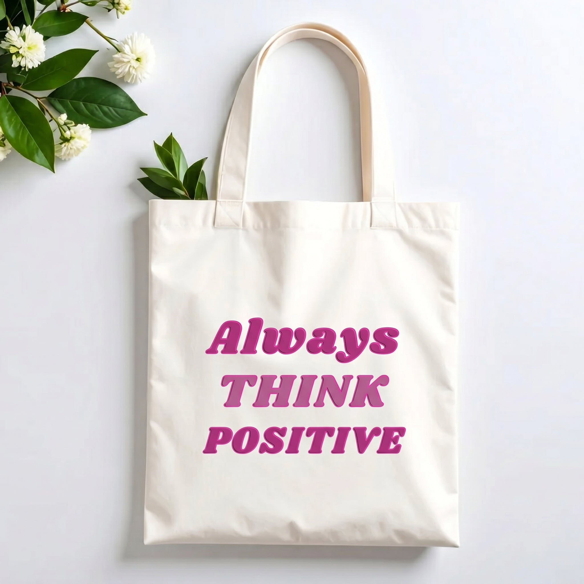 Plovera Co Always Think Positive tote laid flat on pale grey with white blossom and green leaves