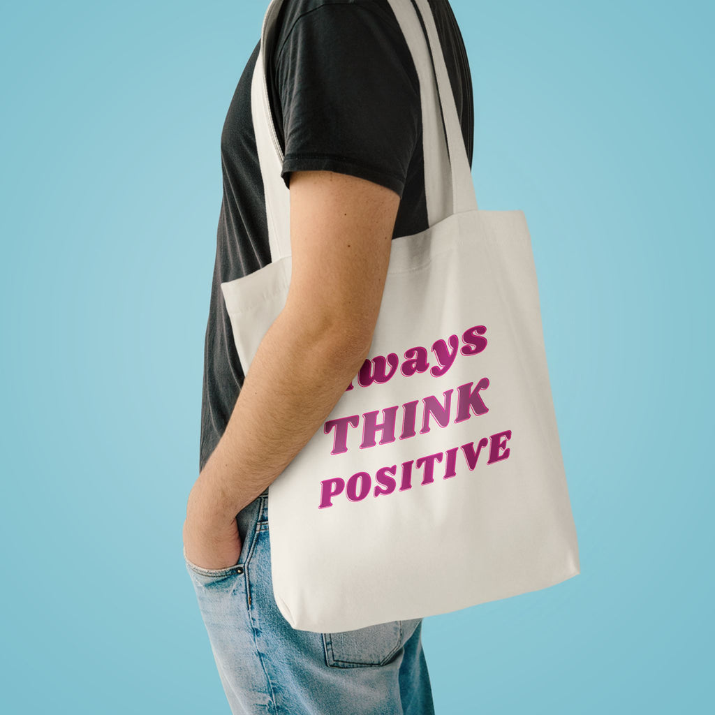 Always Think Positive tote over the shoulder of a person in a charcoal tee against pale blue