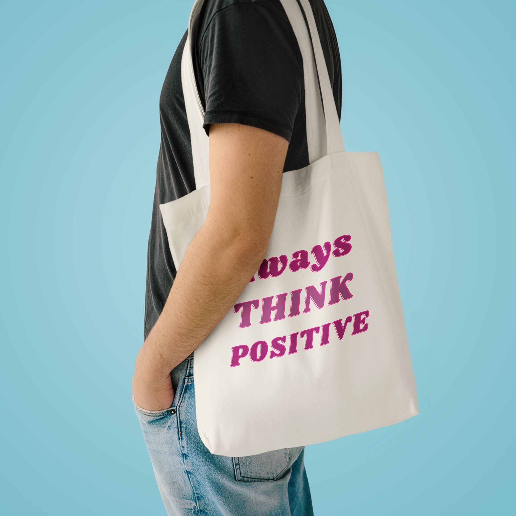 Always Think Positive tote over the shoulder of a person in a charcoal tee against pale blue