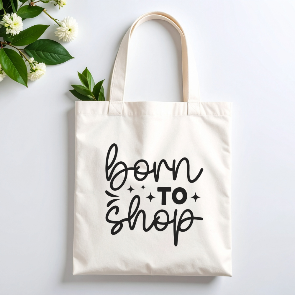 Plovera Co Born To Shop tote laid flat on pale grey with white blossom and green leaves