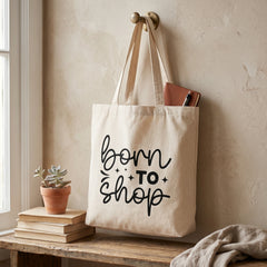 Born To Shop tote hanging from a brass hook with a notebook inside, succulent on books below