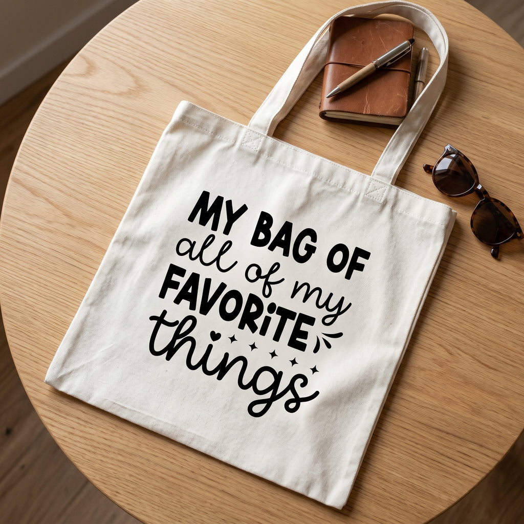 Favorite Things tote on a round oak table with a tan leather notebook, pens and sunglasses