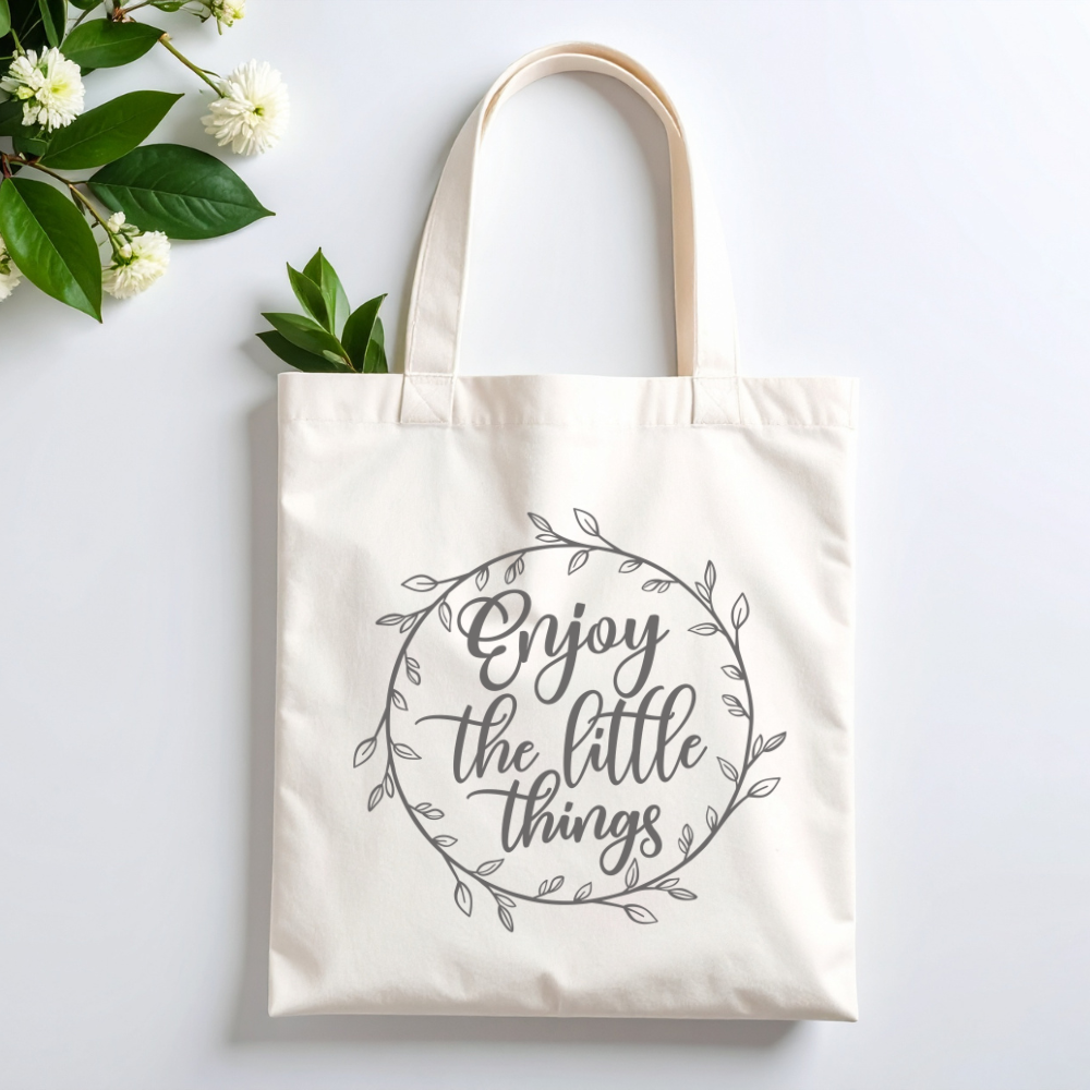 Plovera Co Enjoy the Little Things tote laid flat on pale grey with white blossom and green leaves