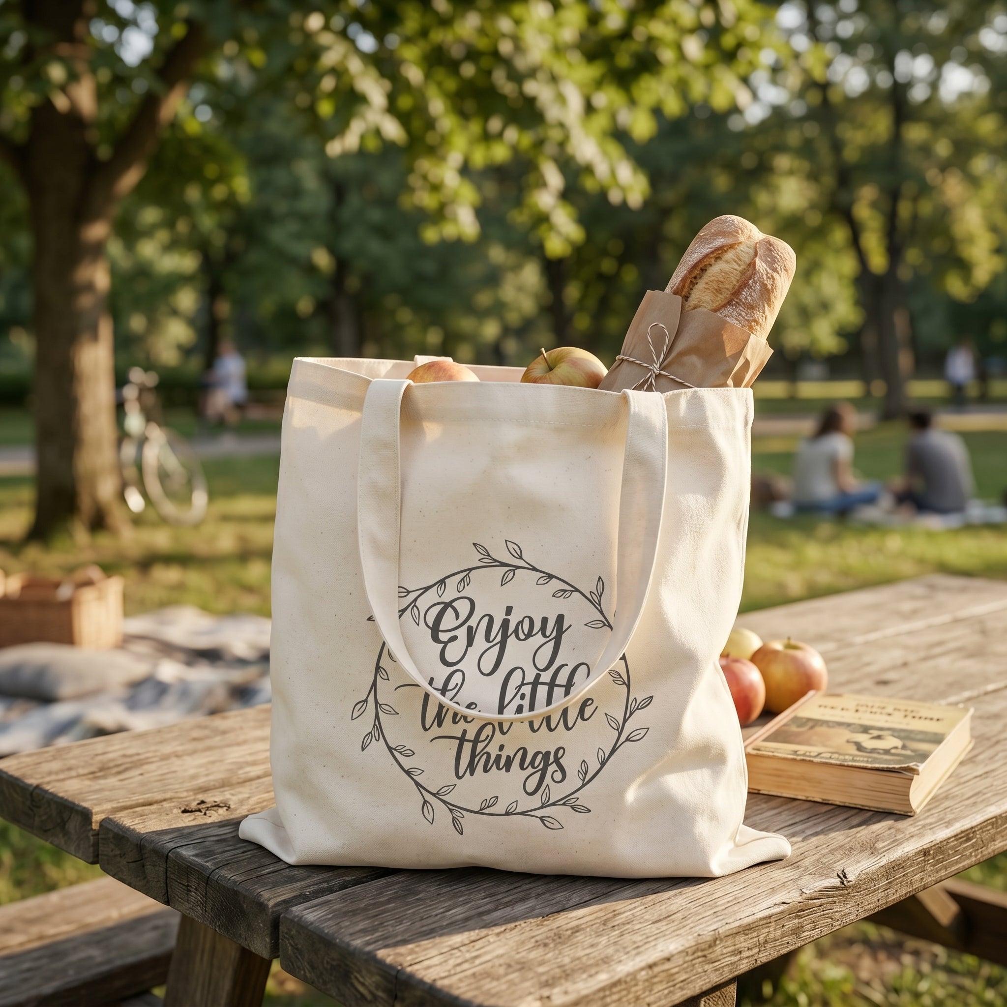 Enjoy the Little Things tote on a picnic table with baguettes and apples inside, park behind