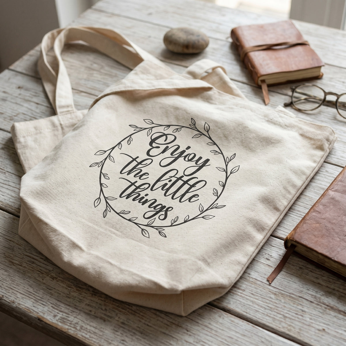 Enjoy the Little Things tote on weathered white boards with leather books, a pebble and round glasses