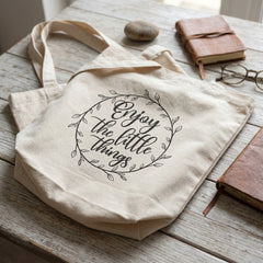 Enjoy the Little Things tote on weathered white boards with leather books, a pebble and round glasses
