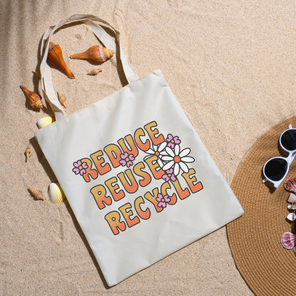 Reduce Reuse Recycle tote on beach sand with seashells, a straw hat and white sunglasses nearby