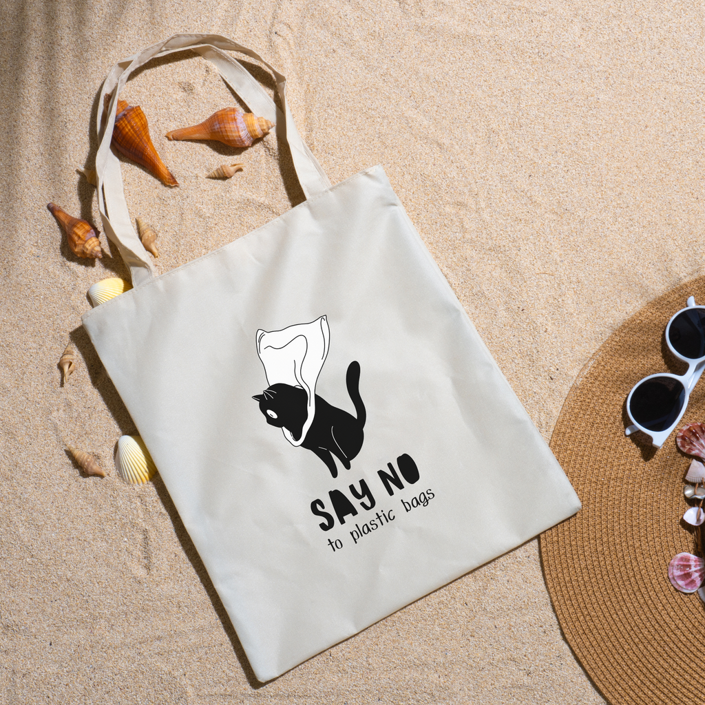 Say No to Plastic Bags tote on beach sand with seashells, a straw hat and white sunglasses nearby