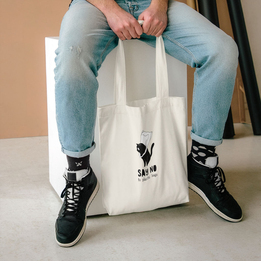 Say No to Plastic Bags tote held between the knees of someone seated in light jeans and high-tops
