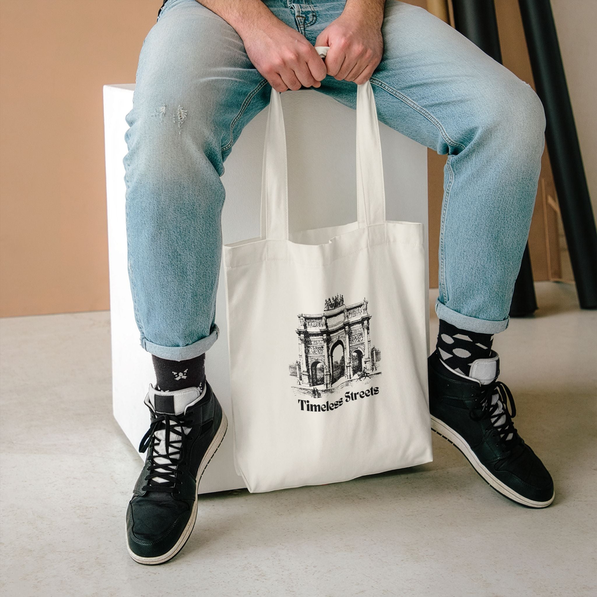 Timeless Streets tote held between the knees of someone seated in light jeans and high-tops