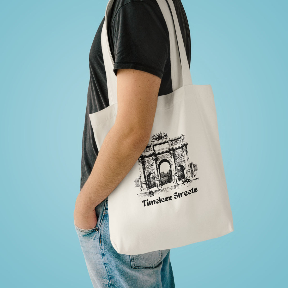 Timeless Streets tote over the shoulder of a person in a charcoal tee against pale blue