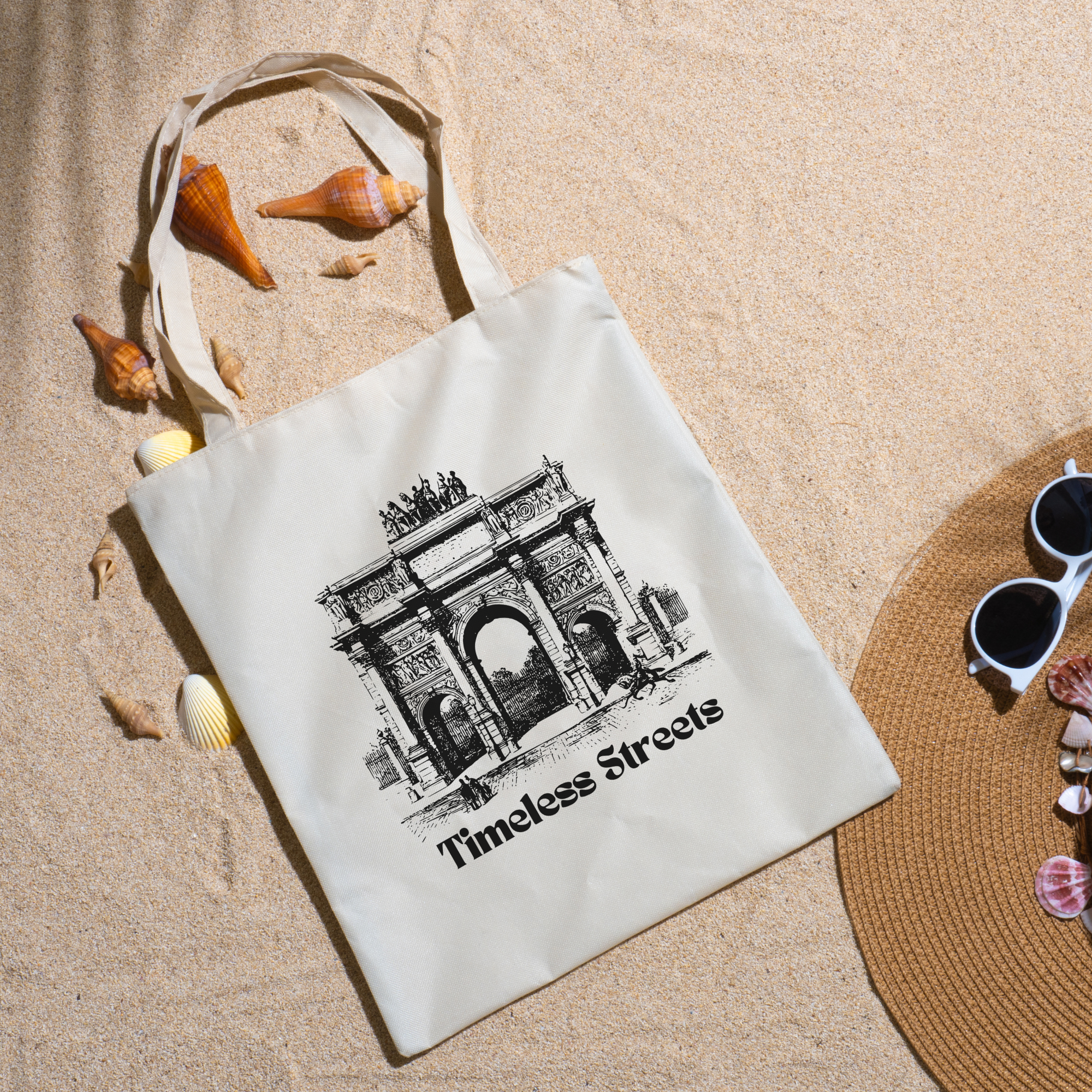 Timeless Streets tote on beach sand with seashells, a straw hat and white sunglasses nearby