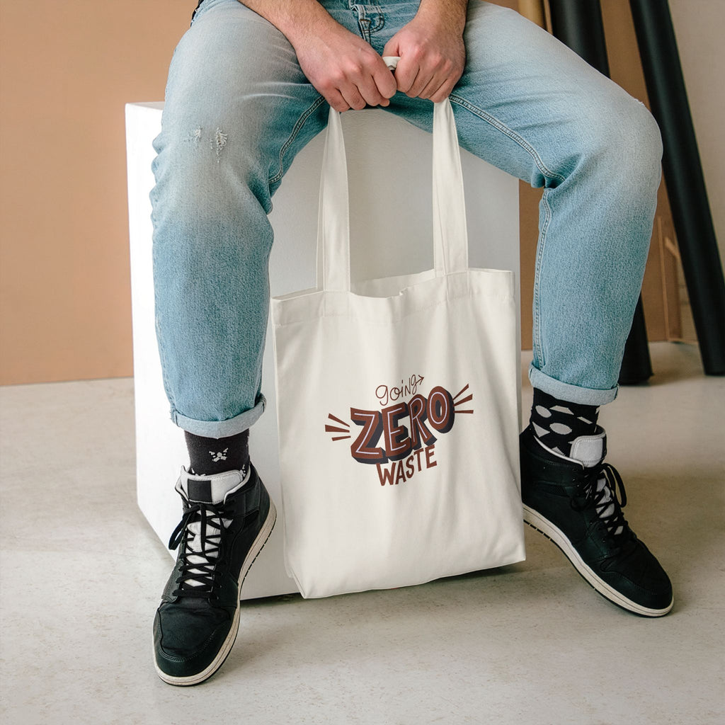 Going Zero Waste tote held between the knees of someone seated in light jeans and high-tops